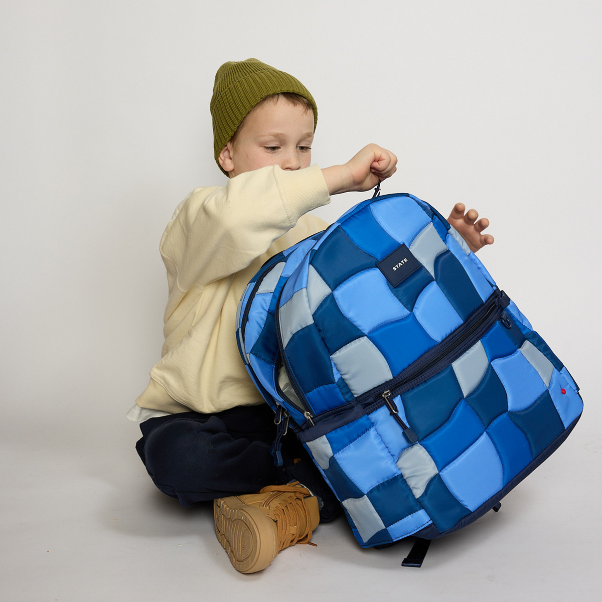 Boy opening Kane Kids Double Pocket Backpack Blue Puffer Check