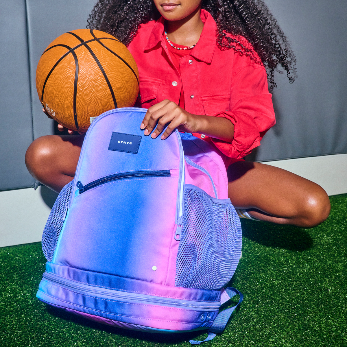 Girl putting basketball in Ozzie Ball Backpack Blue/Pink Gradient