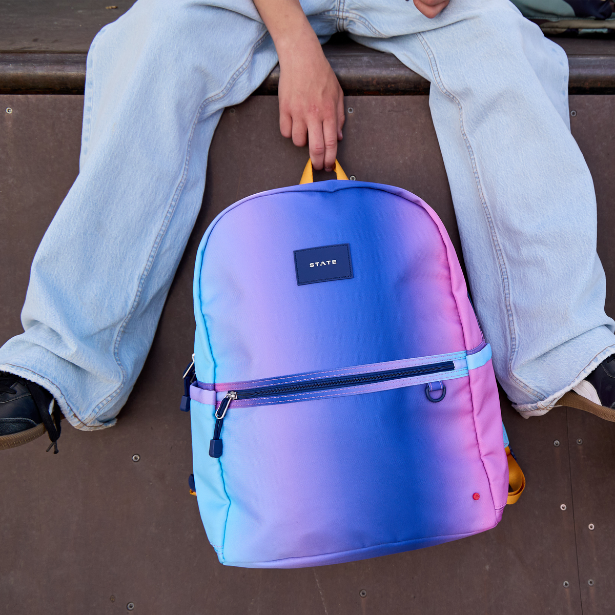 boy holding blue/pink gradient backpack off a ledge